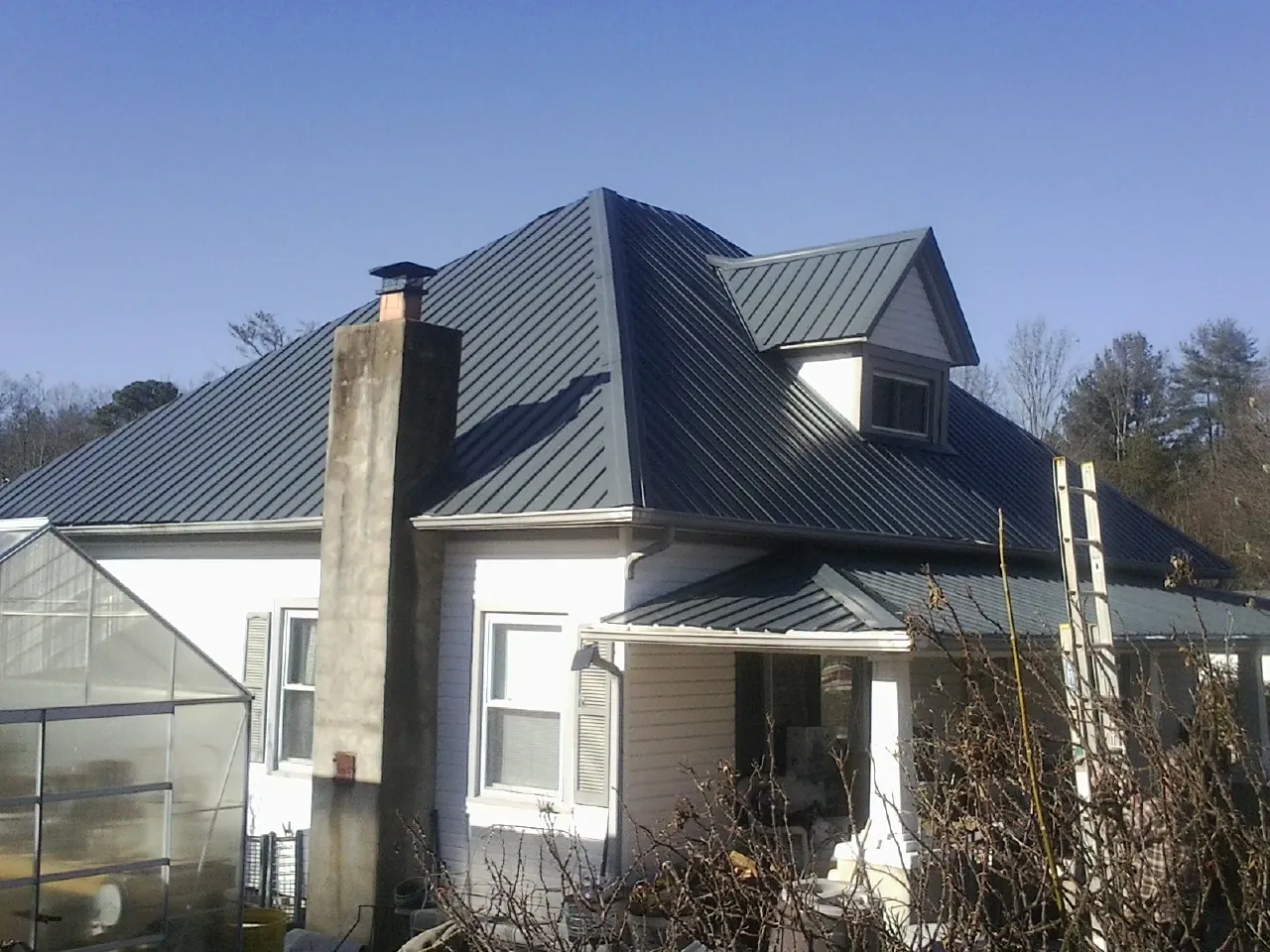 Dark blue standing seam metal roof on a white farmhouse with dormer — Slate & Tile Roof Repair by Roofing Brothers in Zuni