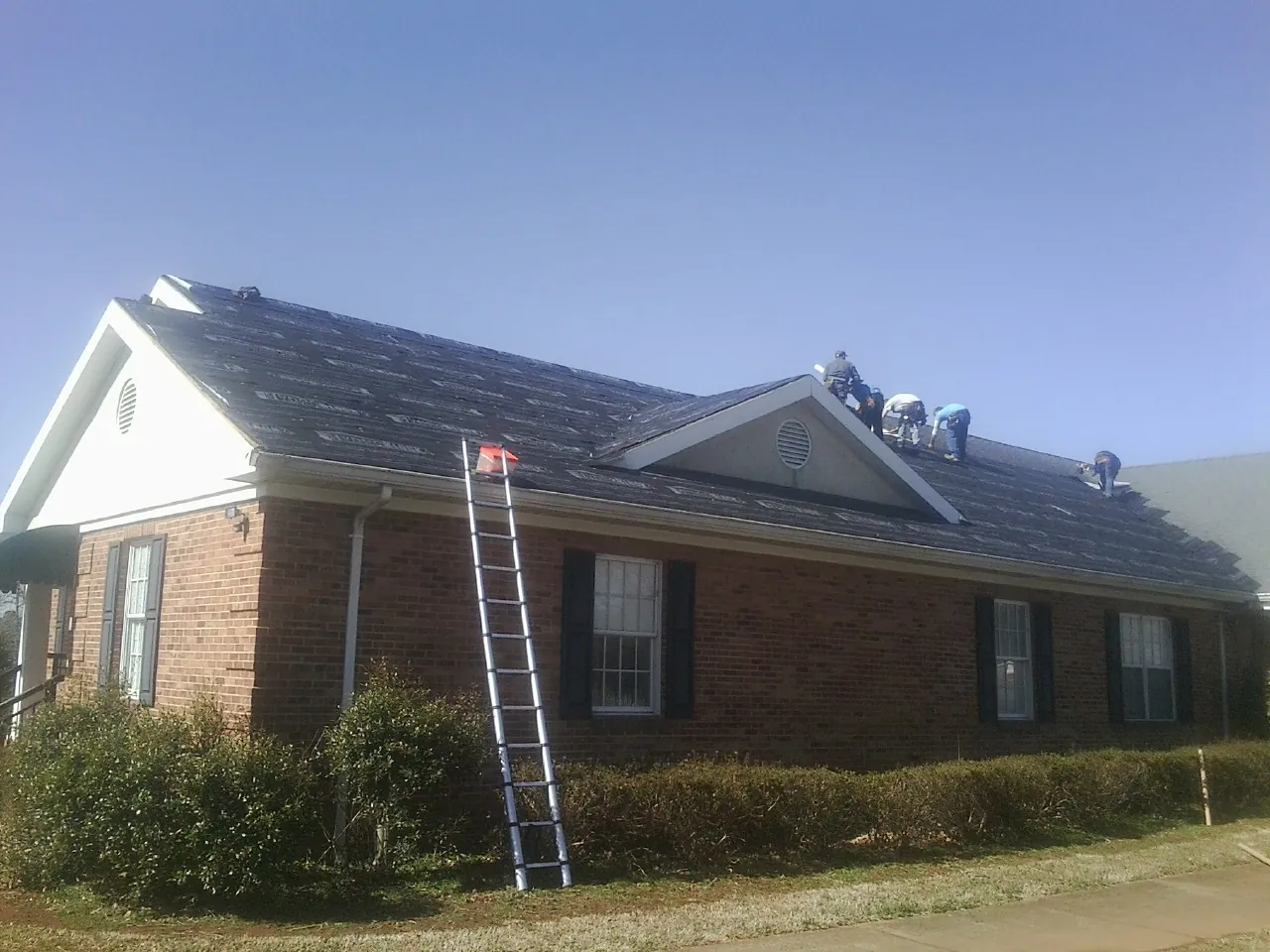 Crew tearing shingles off a brick ranch roof with a ladder set — Metal Roof Repair work by our crew in Zuni