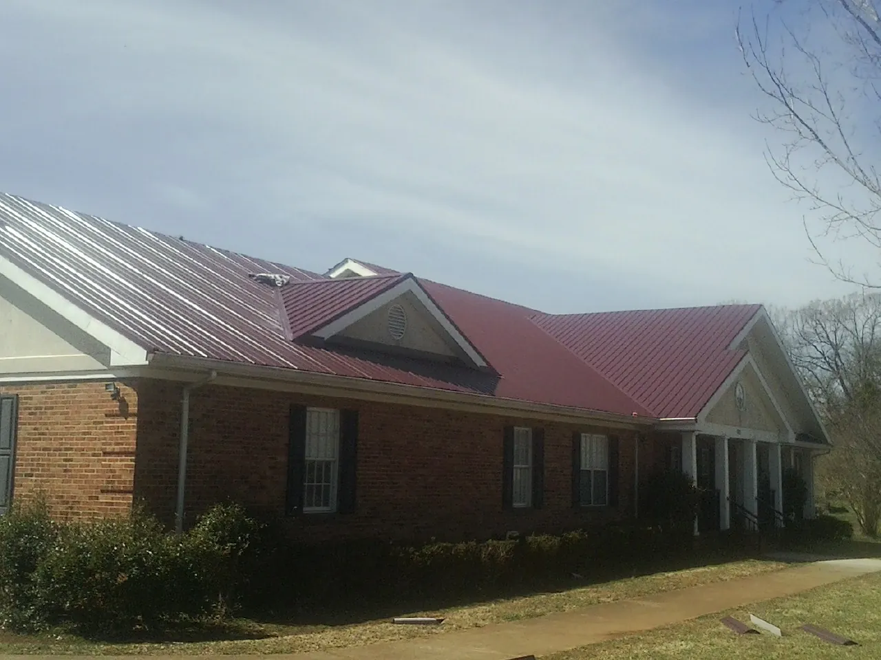 Red metal roof with gabled entries on a long brick building, from a Hail Damage Roof Repair job in Zuni