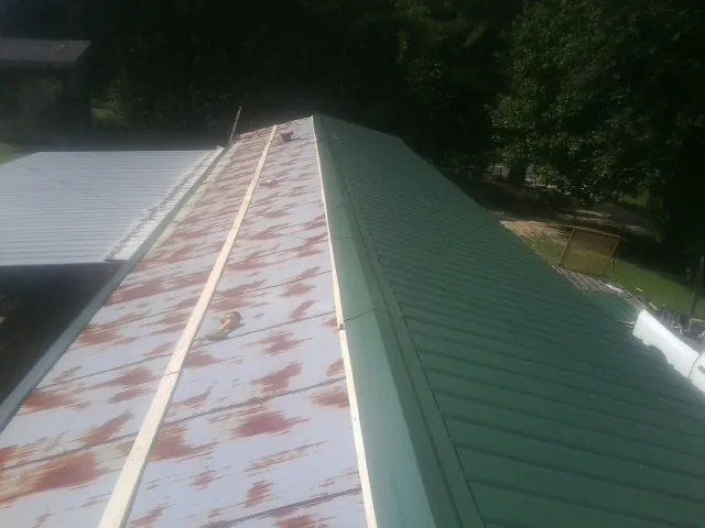 Old rusted panels beside newly installed green metal roofing — Wind Damage Roof Repair by Roofing Brothers in Zuni