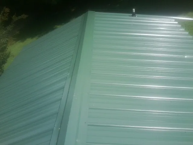 New green metal panels meeting at the ridge of a roof — Flat Roof Repair work by our crew in Zuni