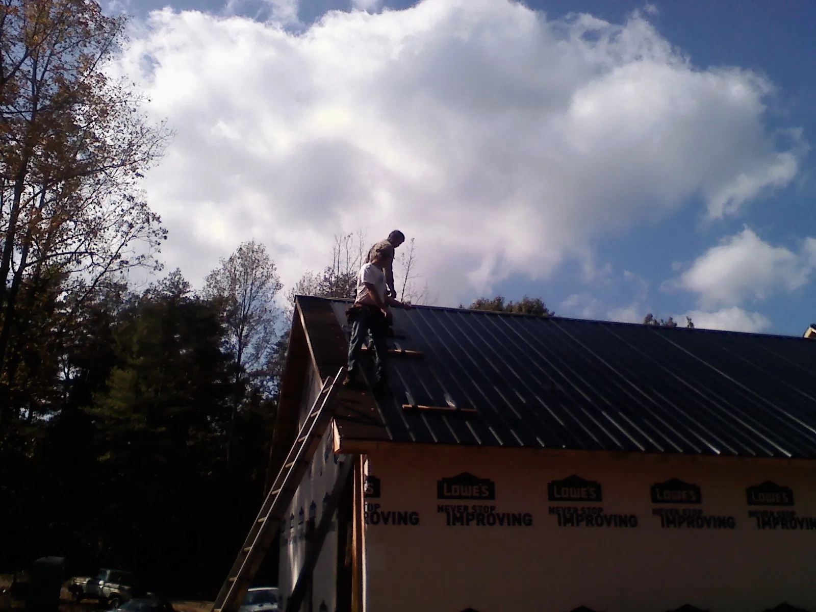 Roofer fastening dark metal panels high against a cloudy sky in Zuni