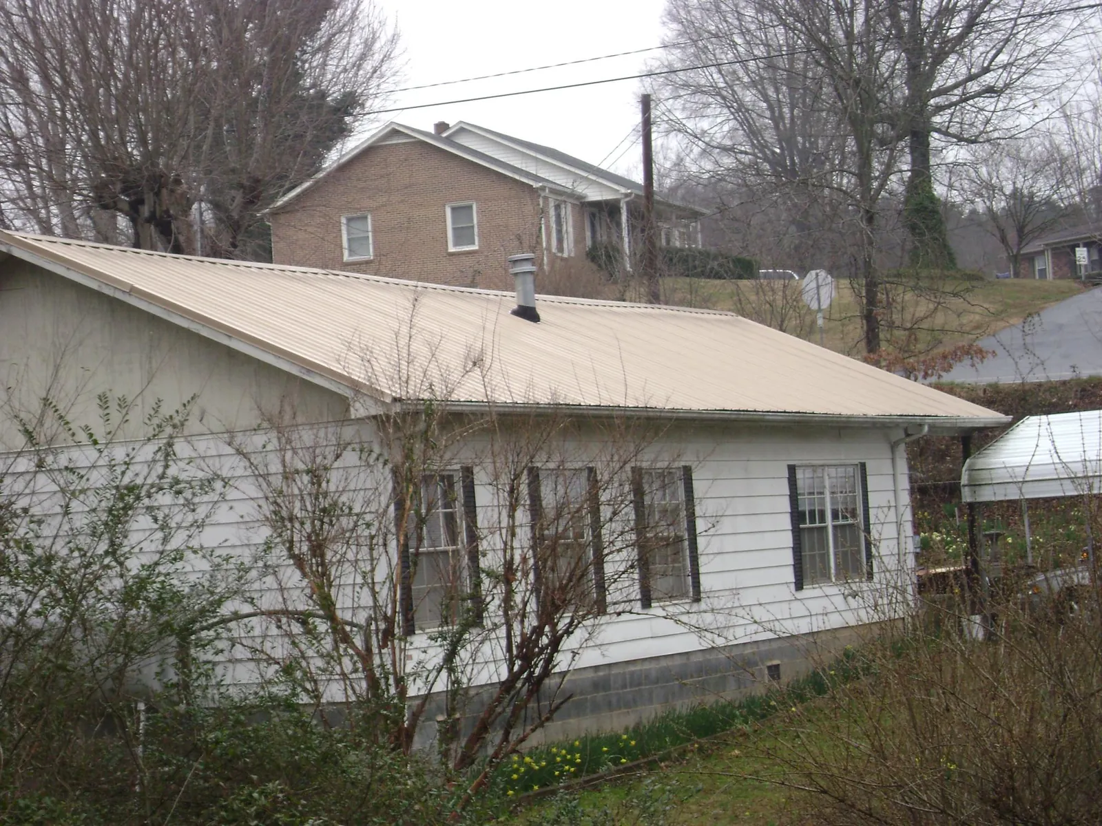 Tan metal roof on a white sided house set into a hillside — Commercial Roofing by Roofing Brothers in Zuni